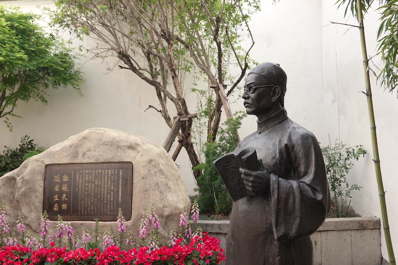 △严复故居里的铜像。他手捧《天演论》，旁边石头上的铜牌写着“物竞天择，适者生存”。（总台央广记者潘毅拍摄）